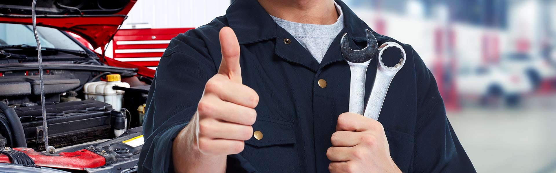 Mechanic holding tools beside an open car hood.